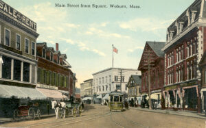 Image of Main Street in Woburn from the Square, showing buildings, a street trolley car, and a horse drawn wagon.